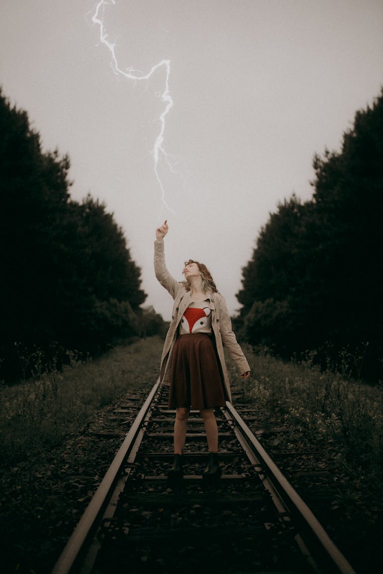 A dramatic shot of a woman posing on train tracks during a lightning storm, showcasing the power of nature.